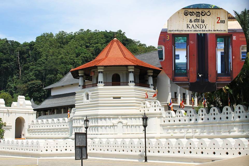 This is a photo of Kandy Railway Station in Sri Lanka, showing a red train stopped at the platform. The station sign is clearly visible, displaying “KANDY” in English, Sinhala, and Tamil. You can see the steps leading into the train, the windows of the carriages, and the lush greenery reflected in them, giving a sense of the scenic surroundings of Kandy.